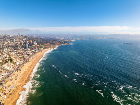 High angle aerial drone shot of Renaca sandy beach coastline with ocean waves and buildings looking towards Vina del Mar city bay and Valparaiso region Chile