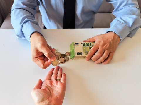 Close-up of male hands passing euro coins and a stack of 100 euro banknotes on a white table.
