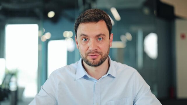 Close-up portrait of serious IT specialist or developer looking at screen during online corporate briefing. Focused businessman having virtual conference or video chat in blurred office interior.