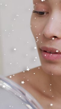 Vertical video: Woman checking skin in round mirror wiping cotton pad while sparkles marking beauty