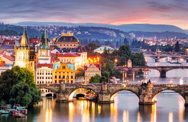 Obraz premium Twilight cityscape featuring multiple bridges over a river in Prague skyline, with historic buildings and street lights.