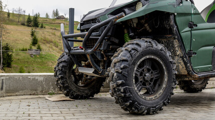Rugged green all-terrain vehicle parked on a paved surface with a hilly landscape © shine.graphics
