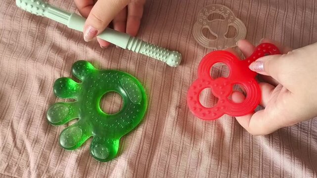 A woman's hands touch teethers for babies' teethers on a crib. Eruption of the first teeth in children