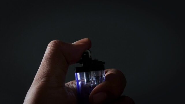 A man lights a lighter. A man holds a lighter in his hand and spins a drum on a dark background. The lighter emits sparks and ignites close up.