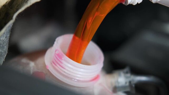 Close Up of Pouring Bright Orange Antifreeze Coolant Fluid into Car Radiator Expansion Tank Under the Hood