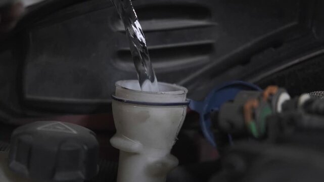 Close Up of Mechanic Pouring Clean Washer Fluid Water into Car Windshield Wiper Reservoir Tank Under the Hood