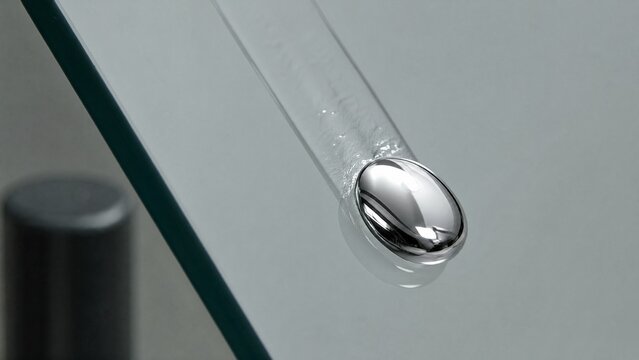 globule. A liquid mercury droplet sliding down a smooth glass surface, leaving a mirrored trail. STEM education sheets, lab safety posters, designed for biotech research communications.