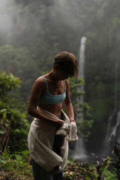 Young woman undressing by misty waterfall in tropical jungle, Bali
