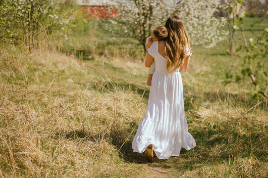 Mother carrying toddler through blooming spring orchard in park
