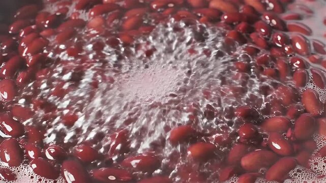 An extreme close up shows red beans actively boiling in a pot of water. Numerous air bubbles rapidly rise to the surface.