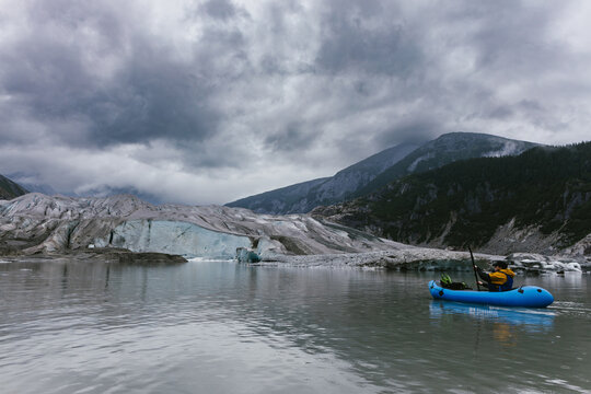 Man paddles kayak up to glacier with ice and mountains