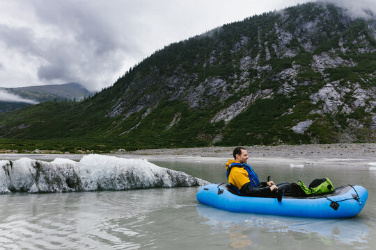 Man in blow up kayak paddling in lake with mountain in Alaska