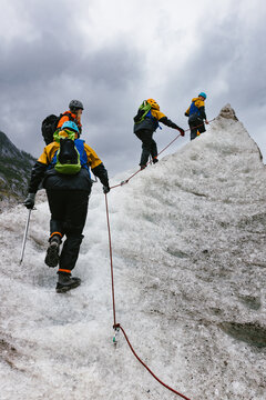 People climbing ice hill with spikes and rope on glacier
