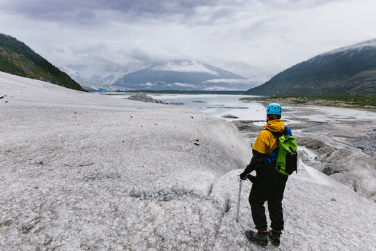Man with ice spikes hikes on glacier with lake and mountains