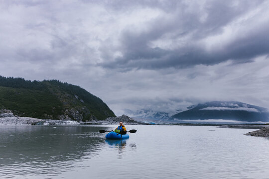 Man paddles kayak on glacial lake with snowy mountains