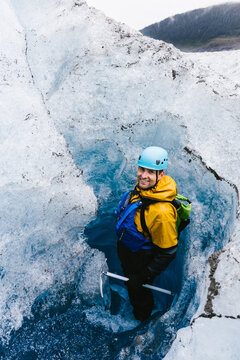 Man in helmet smiling in hole in glacier on adventure on vacation