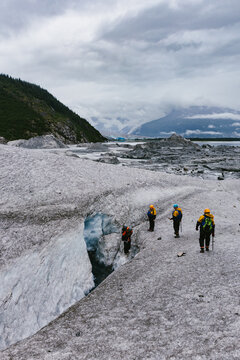 People hike on glacier over looking lake and snow capped mountains