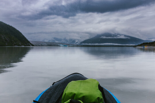 Edge of kayak looking over glacial lake with mountains and clouds