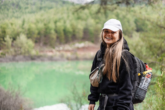 Happy young woman smiling while hiking by a green lake