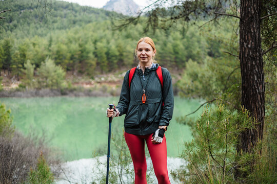 Woman hiker with trekking pole stands near lake