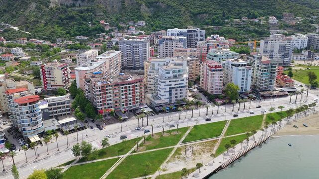 Aerial video of the urban waterfront in Vlora, Albania, showcasing a dense row of modern multi-story apartment complexes and the coastal boulevard. 