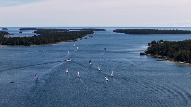 Aerial view of Lake Huron in Hessel, Michigan with multiple sailboats cruising on calm waters amidst wilderness and scattered islands.