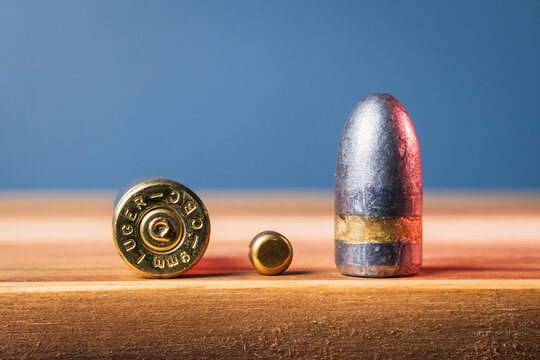 BALTIC STATES - MAY 26, 2026: Macro view of disassembled 9mm Luger ammunition components showing a brass case headstamp, primer, and lead bullet on wood.