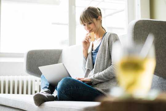 Smiling woman sitting on couch with credit card and laptop