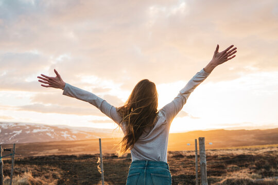Iceland, young woman with raised arms at sunset