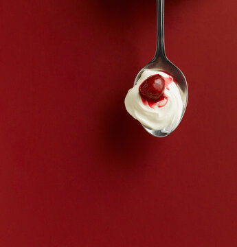 Yogurt and cherry in spoon on red background