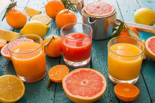 Glasses of orange juice, grapefruit juice and multivitamine juice, juice squeezer and fruits on wood