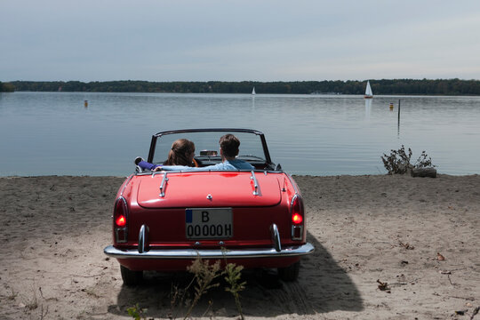 Germany, Berlin, Lake Wannsee, Young couple in cabriolet looking at lake, rear view