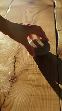Overhead ecu video of light brown wooden planks with intricate grain, bathed in soft golden hour sunlight. A hand places a polished river stone. Concept of sustainable living