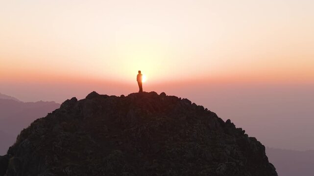 4K scenic sunrise drone shot of a boy standing atop a rugged Himalayan mountain in Uttarakhand, India.
