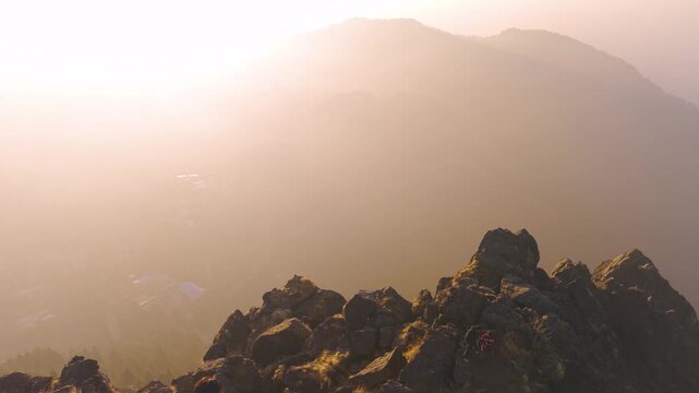 4K aerial drone footage of a boy enjoying panoramic sunrise scenery from a rocky mountain summit in Uttarakhand.