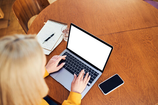 Woman typing on laptop with blank screen at home wooden table