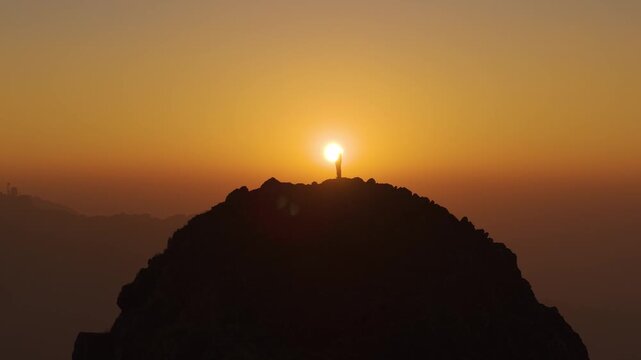4K aerial view of a boy enjoying peaceful sunrise moments on a dramatic rocky cliff in Uttarakhand, India.