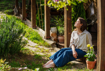 Mature woman sitting on a terrace with her eyes closed, enjoying the warm sun on her face on a beautiful summer day. © olezzo