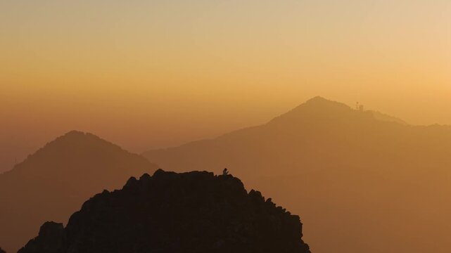4K aerial footage of a boy admiring panoramic Himalayan sunrise views from a rocky cliff.