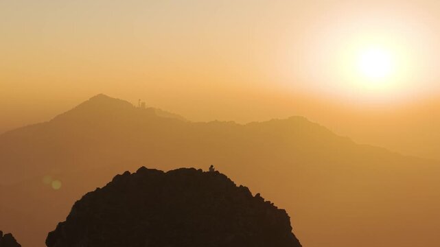 4K sunrise drone shot of a traveler standing on a mountain ridge with colorful skies over Uttarakhand.