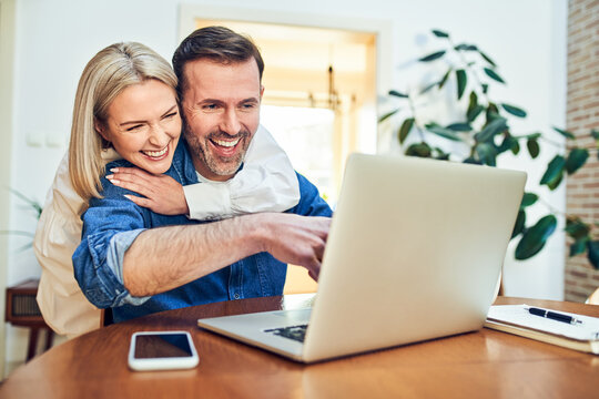 Couple laughing together while using laptop at home
