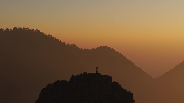 4K aerial view of a young traveler enjoying sunrise scenery from a mountain top in Uttarakhand.