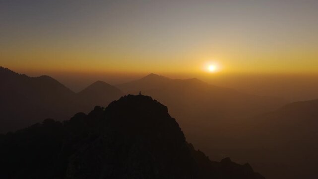 4K aerial shot of a boy enjoying serene sunrise moments on a mountain cliff in Uttarakhand.