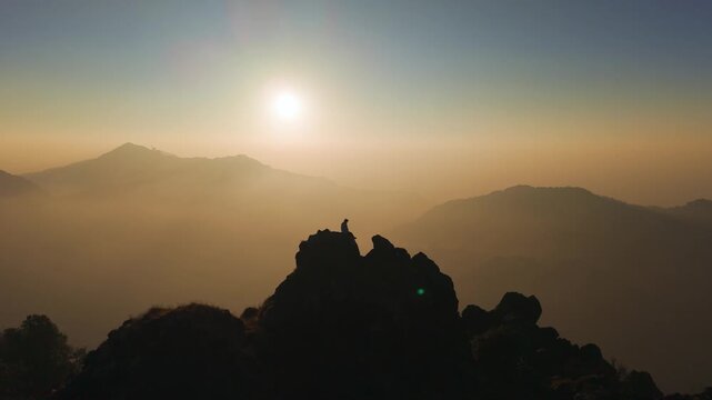 4K cinematic drone view of a traveler enjoying the rising sun from a rocky Himalayan cliff.