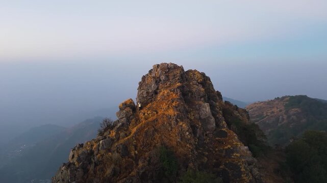4K aerial sunrise footage of a boy climbing a steep Himalayan cliff with panoramic mountain scenery in Uttarakhand.