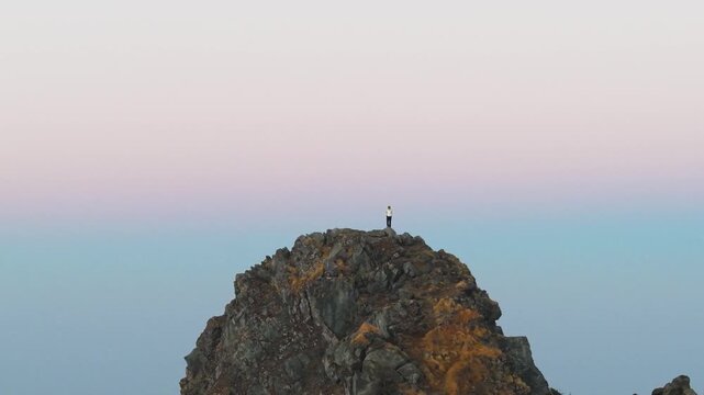 4K aerial 360 cinematic view of a traveler enjoying sunrise from a rocky Himalayan summit in Uttarakhand, India.