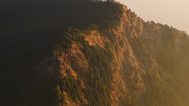 4K aerial close-up shot of rugged rocky mountains glowing under warm sunlight with vibrant orange and dusty tones in Uttarakhand, India.