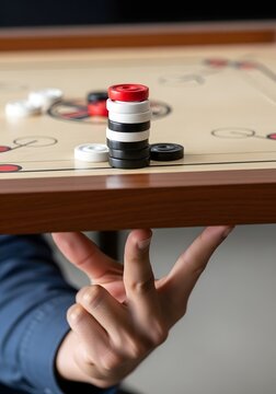 Close up of a hand balancing a stack of carrom coins under the indoor game board
