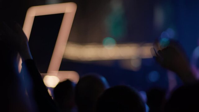 Fan holds up a bright glowing square LED frame during a live concert, with colorful blurred stage lights visible in the background