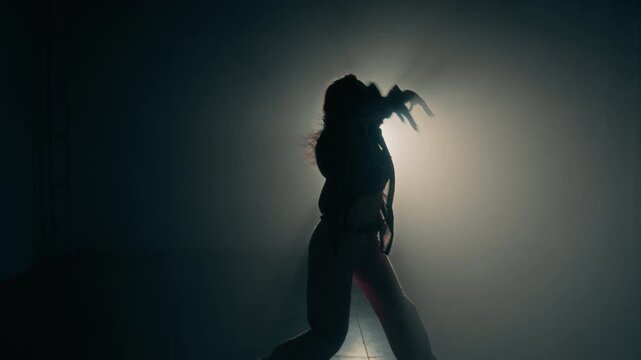 Artistic dance performance of young female dancer silhouette against glowing backlight highlighting expressive body movement in dark studio, copy space